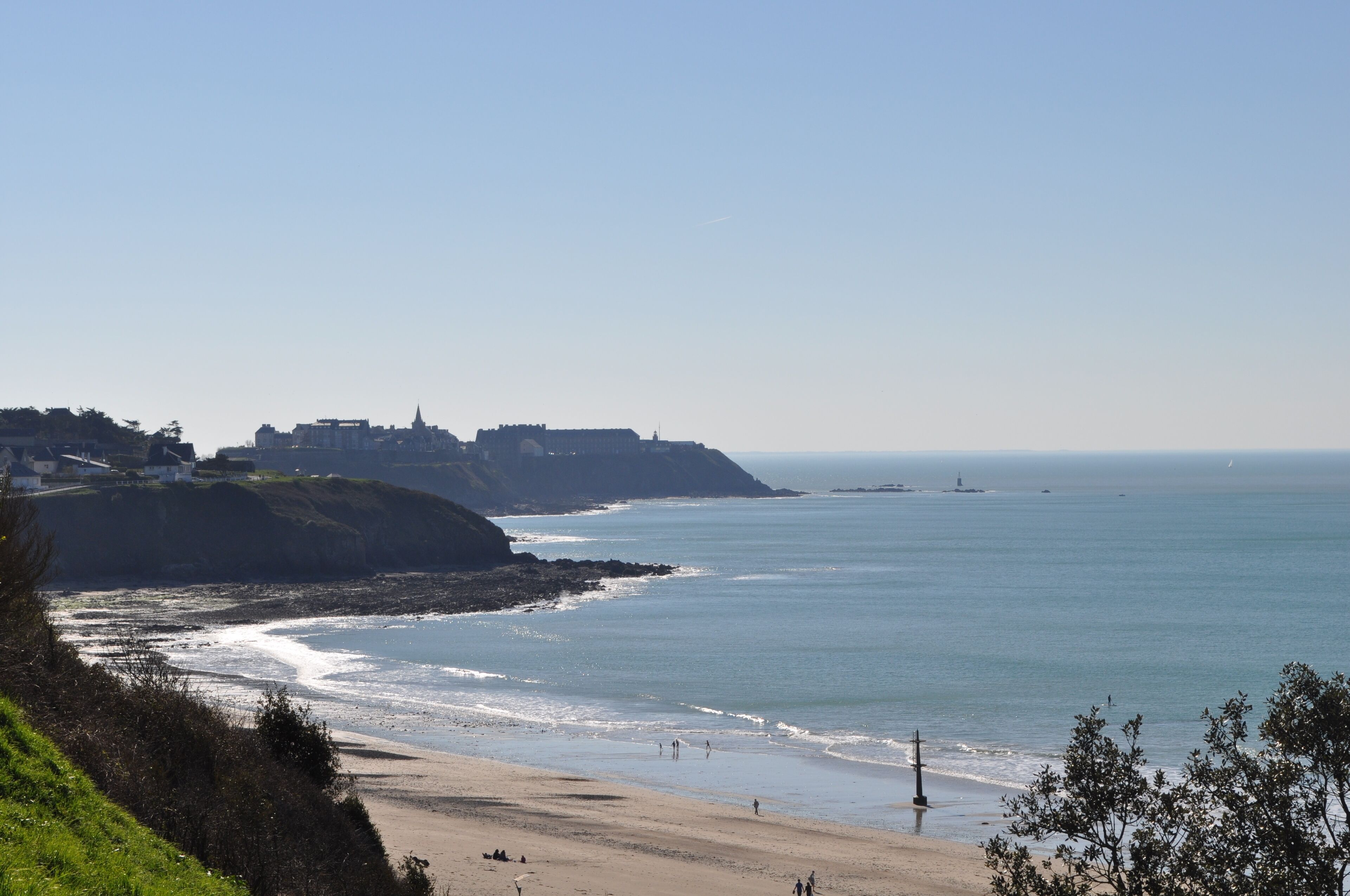 A coastal view with a beach, a cliff, and a distant building.