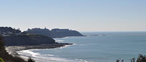 A coastal view with a beach, a cliff, and a distant building.