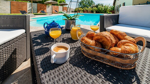 A wicker table with a basket of croissants, a cup of coffee, and a glass of orange juice by a poolside. - Spacious 410m² 3-star cottage: private heated pool, spa, canoes and paddl (Trentels)