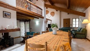 A cozy living room with a wooden dining table, chairs, a green sofa, and a balcony with wooden railings. - Spacious 410m² 3-star cottage: private heated pool, spa, canoes and paddl (Trentels)