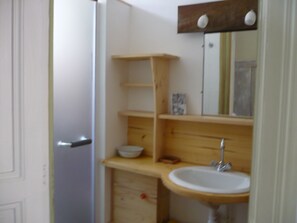 Une salle de bain avec un lavabo blanc, des étagères en bois et un miroir.