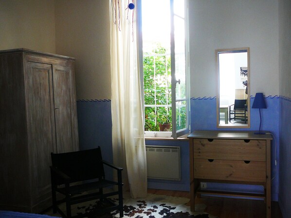 Ein Zimmer mit einem Holzkabinett, einem Sessel, einer Kommode und einem Fenster mit Vorhängen.