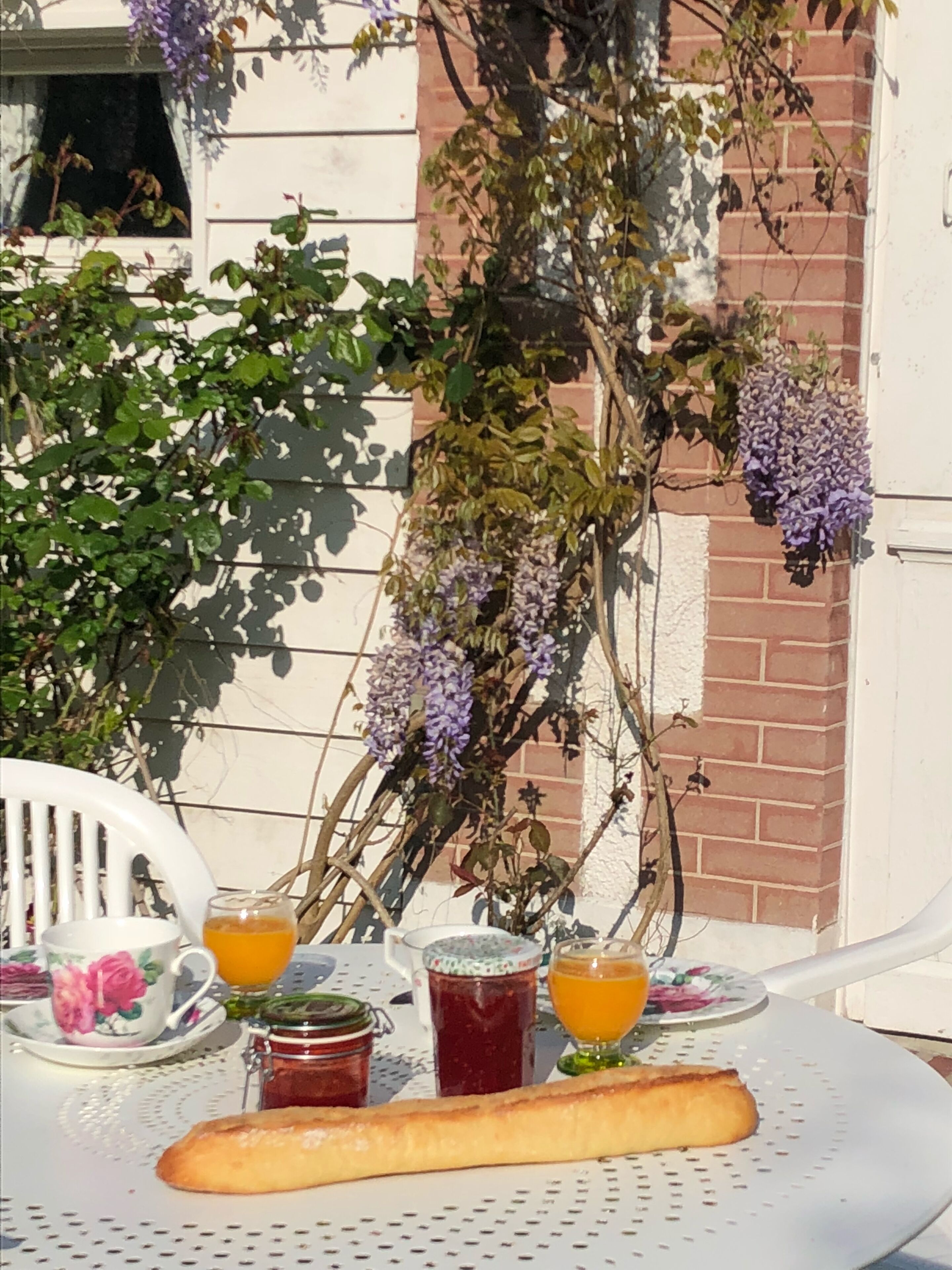 A table with a baguette, two cups of orange juice, and two jars of jam.