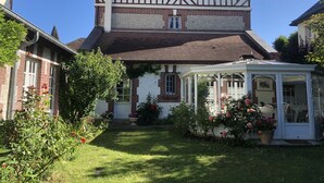 Una casa de estilo Tudor con un jardín cuidado, un invernadero y una chimenea visible.