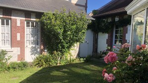 Un jardín residencial con césped, plantas florecientes y una casa de ladrillo con ventanas blancas.