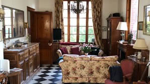 Una habitación con piso a cuadros, muebles de madera, un sofá floral y una araña.