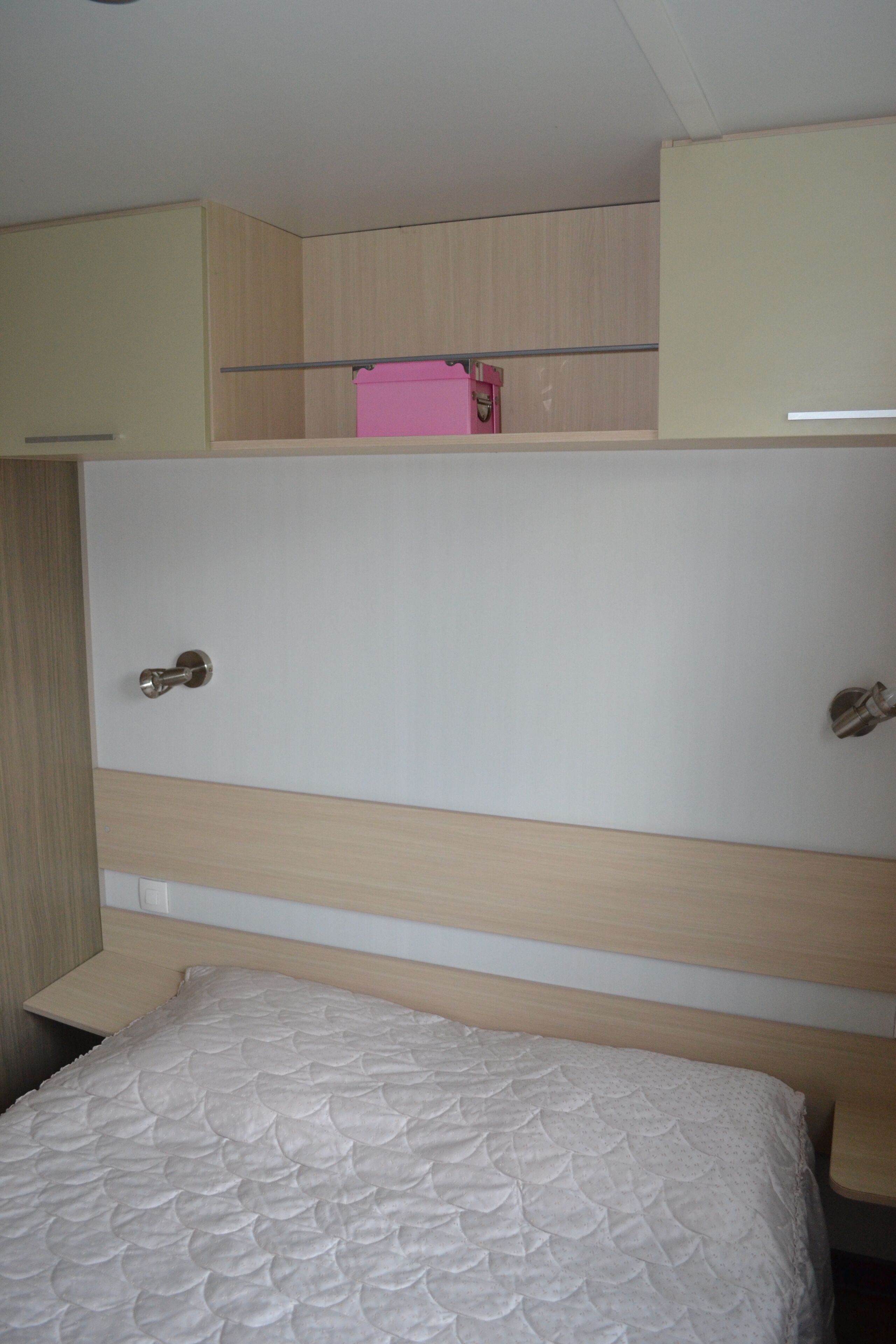Une chambre avec un lit superposé, une tête de lit en bois, une table de chevet et un sac rose sur le lit du haut.