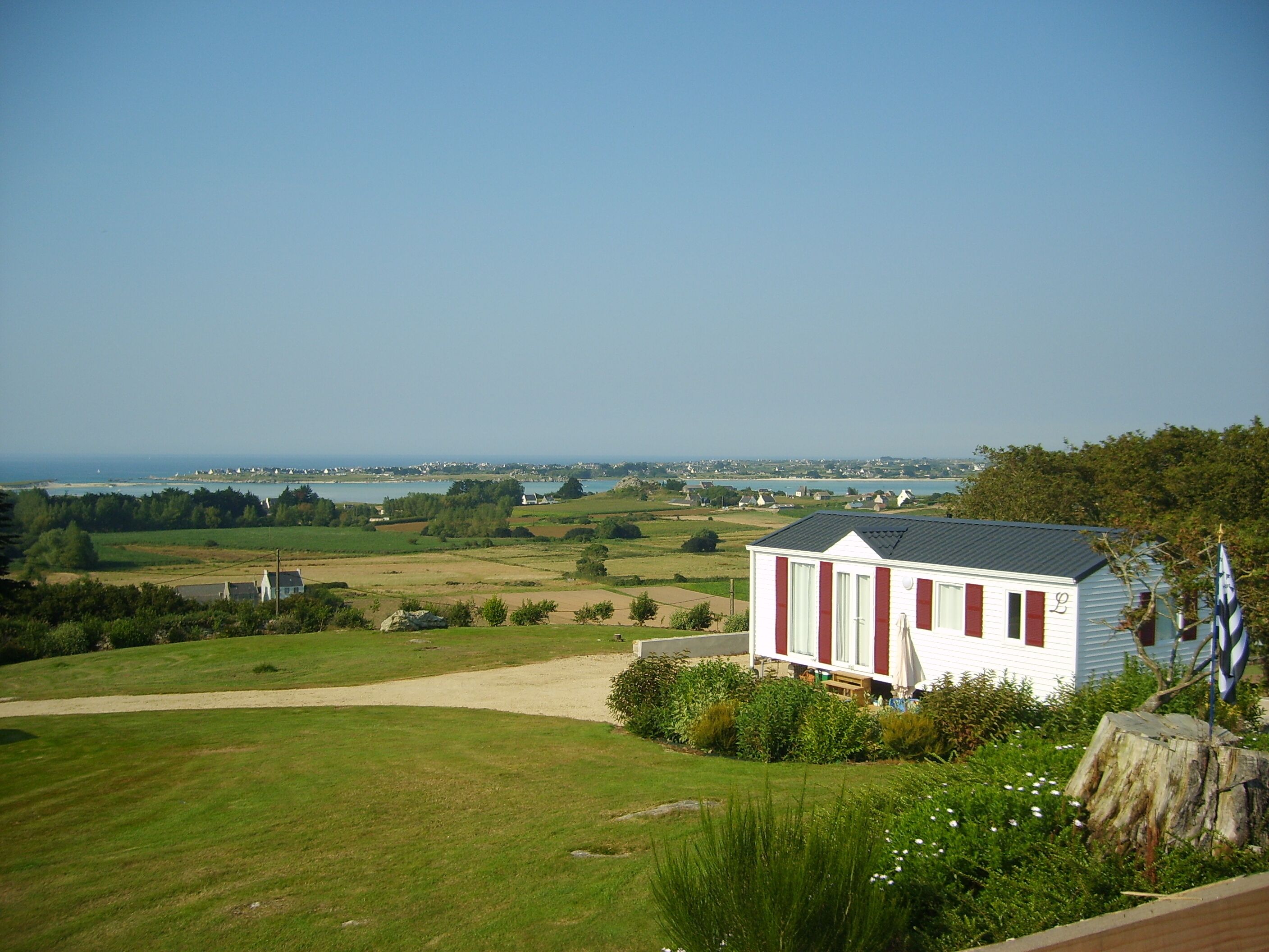 A single-story house with a red and white exterior, situated on a grassy hill overlooking a coastal landscape with a clear sky.