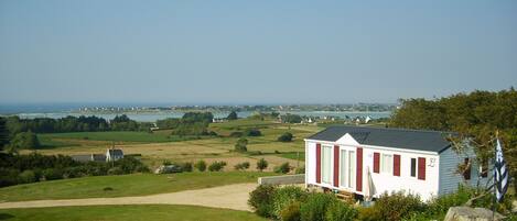 A single-story house with a red and white exterior, situated on a grassy hill overlooking a coastal landscape with a clear sky.