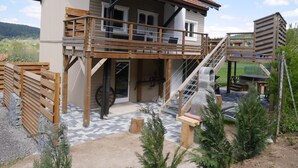 Ein zweistöckiges Haus mit Balkon, Holzterrasse und einer Treppe, die zu einer oberen Ebene führt.