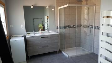 Une salle de bain moderne avec une douche à l’italienne, un meuble-lavabo avec un miroir et un petit lave-linge.