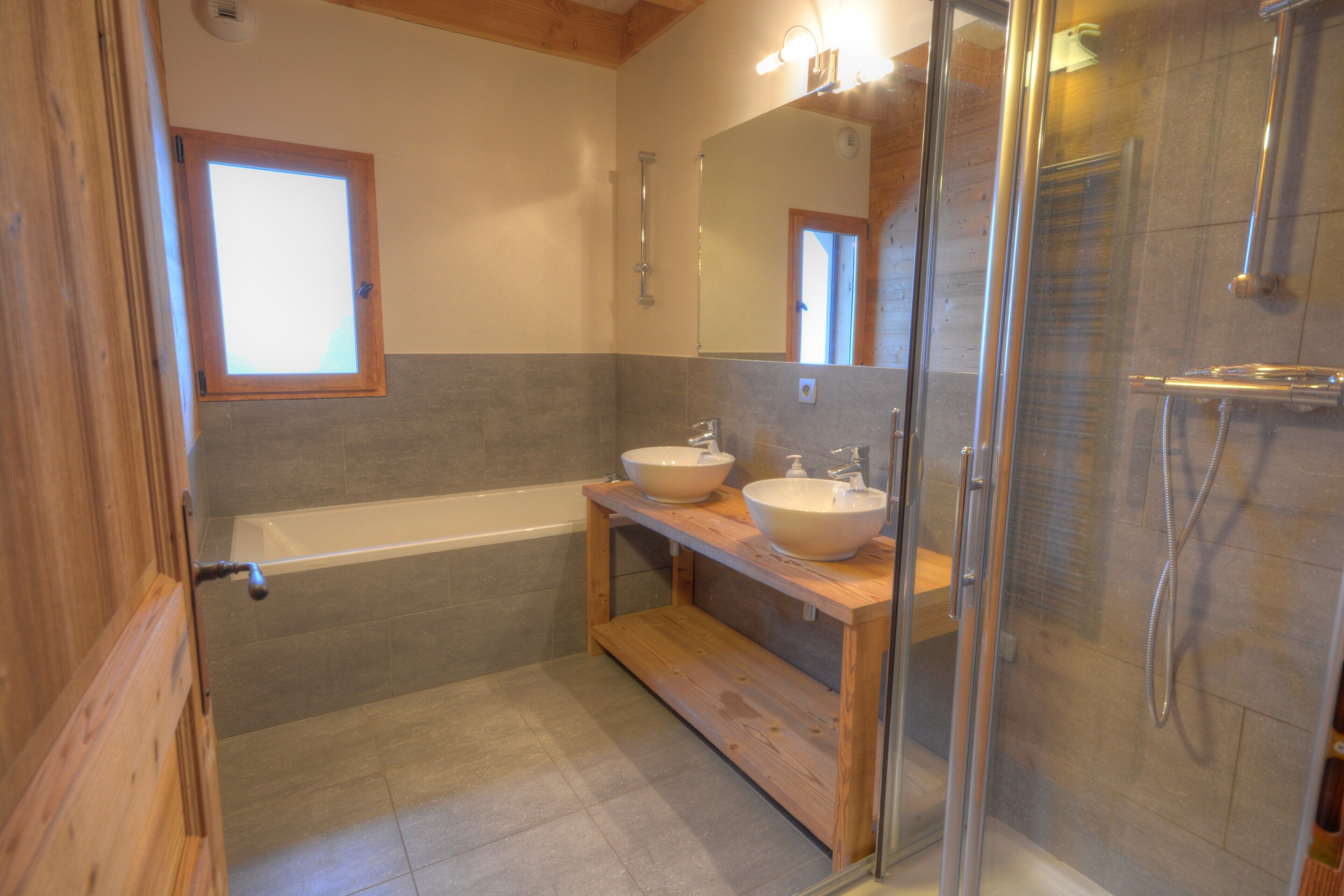 Ein Badezimmer mit einer Badewanne, zwei Waschbecken, einer Duschkabine aus Glas und Holzelementen.