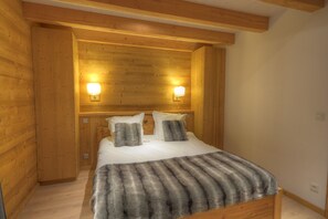 A wooden-paneled bedroom with a bed, two wall-mounted lights, and a fur throw. - Grand Massif 8 bedrooms/8 bathrooms sauna, pool table, walk to village & gondola (Morillon)