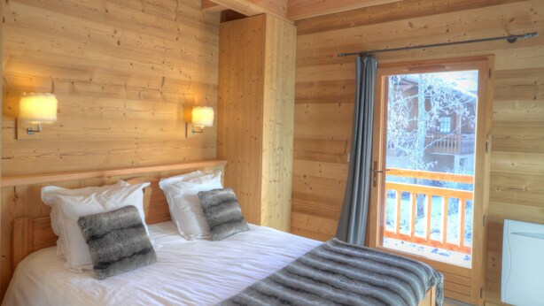 A wooden cabin bedroom with a bed, two wall-mounted lights, and a window with a view of a building outside. - Grand Massif 8 bedrooms/8 bathrooms sauna, pool table, walk to village & gondola (Morillon)