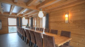 A wooden-paneled dining area with a long table and chairs, large windows, and a hanging light fixture. - Grand Massif 8 bedrooms/8 bathrooms sauna, pool table, walk to village & gondola (Morillon)