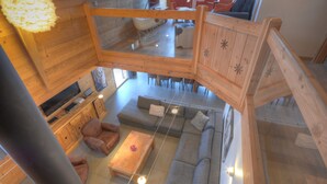 A spacious loft-style living area with a high ceiling, wooden beams, a large gray sectional sofa, a wooden coffee table, and a dining area with red chairs. - Grand Massif 8 bedrooms/8 bathrooms sauna, pool table, walk to village & gondola (Morillon)