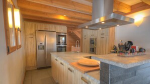 A modern kitchen with wooden cabinets, a large island, stainless steel appliances, and a stone countertop. - Grand Massif 8 bedrooms/8 bathrooms sauna, pool table, walk to village & gondola (Morillon)