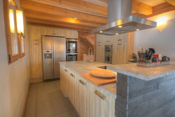 Una cocina moderna con armarios de madera, una isla grande, electrodomésticos de acero inoxidable y encimera de piedra.
