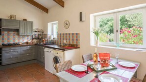 A kitchen with a dining area, a washing machine, and a window with a view of flowers.