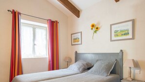 A double bed with a grey headboard and footboard, two bedside tables with lamps, a window with curtains, and two framed pictures on the wall.