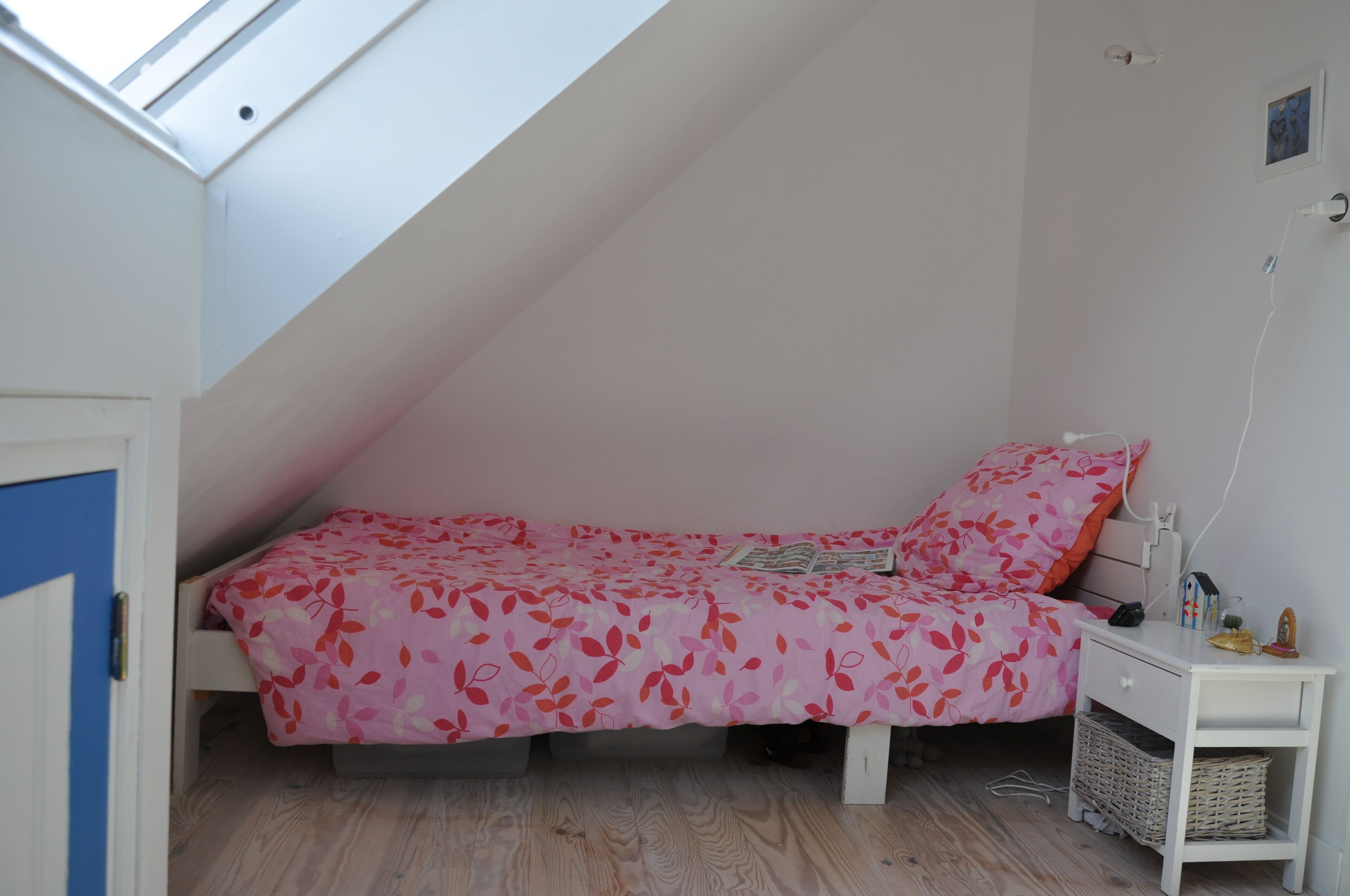 A small, single-bed room with a sloped ceiling and a skylight.