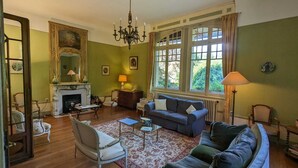 Un salon traditionnel avec une cheminée, un lustre et une grande fenêtre agrémentée de rideaux.