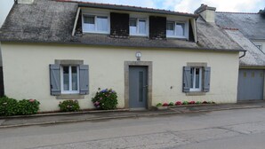 Un immeuble de deux étages avec une façade beige, une porte grise et des volets aux fenêtres.