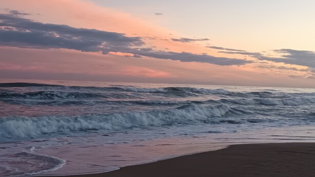 Ein Strand mit Wellen und einem Sonnenuntergangshimmel.