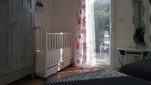 Ein Zimmer mit einem Kinderbett, einem Kleiderschrank, einem Bett und einem Fenster mit Vorhängen.