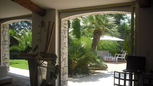 A spacious patio with a stone archway leading to an outdoor area featuring a palm tree, a table with chairs, and a TV. - Starry EDEN (Saint-Paul-De-Vence)