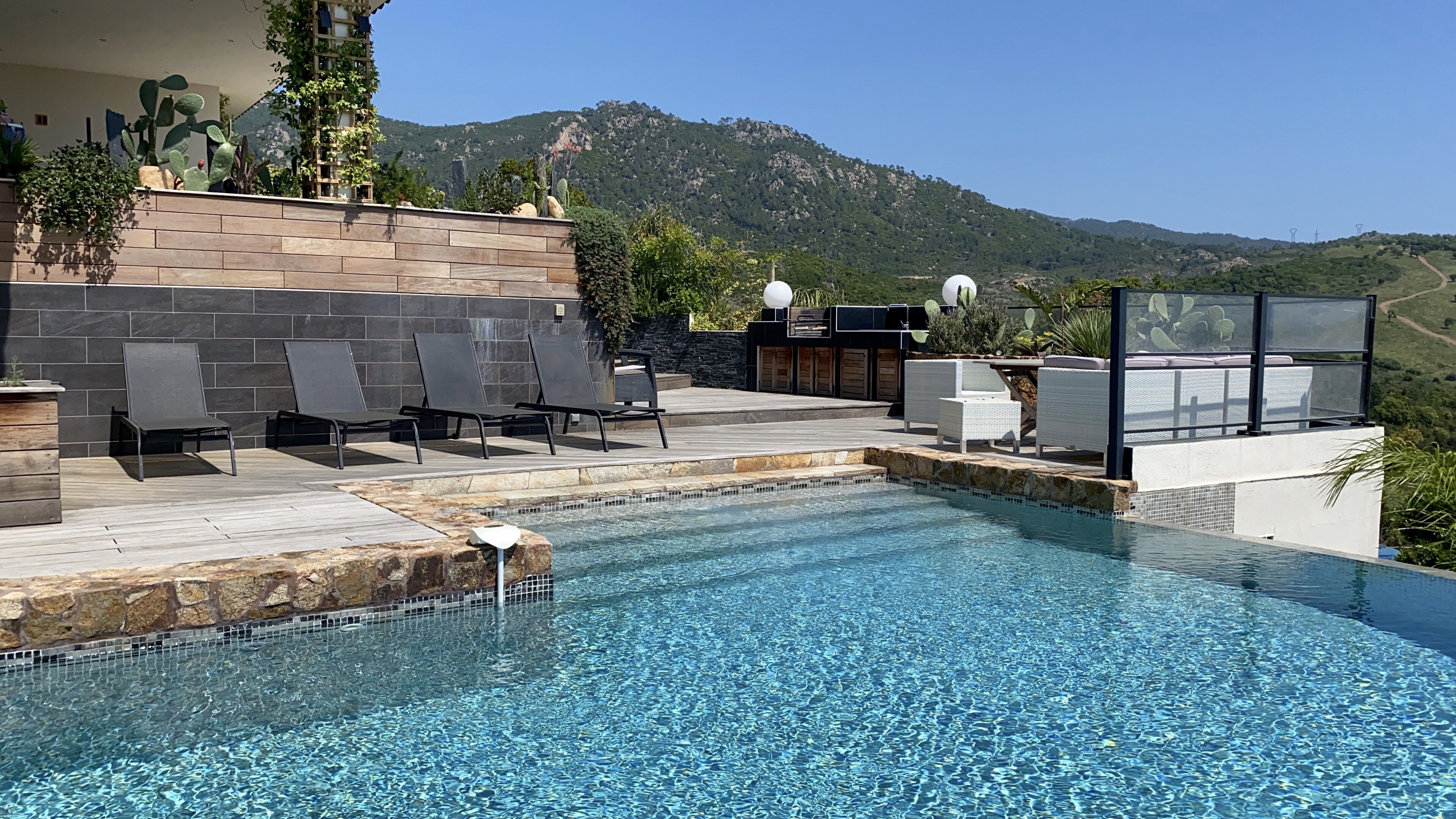Un espace piscine doté de chaises longues, d’un mur en pierre et offrant une vue sur les montagnes.