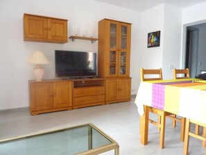 A living room with wooden cabinets, a television, a dining table with chairs, and a glass-top coffee table. - Ground floor with large terrace Beach at 350m Center and Port at 15mn by foot (Cambrils)