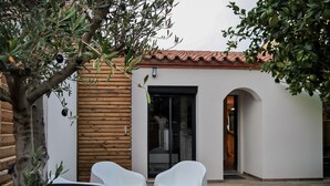 An outdoor patio with a wooden table and two white chairs, a tree with olives, and a building with a tiled roof and a glass door. - Villa with 2 private pools - close to the beach (Bompas)
