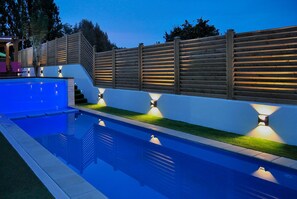 A swimming pool with a wooden fence and built-in lighting, surrounded by a well-maintained lawn.