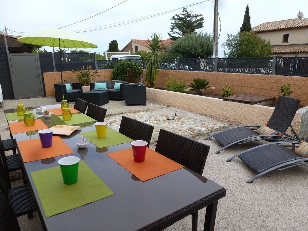 En udendørs patio med borde og stole, en grøn parasol og en stenvæg.