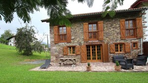 A stone building with wooden shutters, a patio with seating, and a view of a hill.