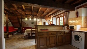 A rustic kitchen with wooden cabinets, a washing machine, and a dining area with a red sofa.