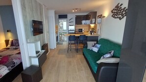 Et moderne opholdsrum med seng, grøn sofa, et tekøkken og et TV ophængt på væggen.