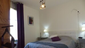A bedroom with a bed, nightstands, a hanging light fixture, a painting, and a window with curtains. - Very nice apartment, luxury residence, garage, WIFI, 2 free bicycles. (Saint-Valery-Sur-Somme)