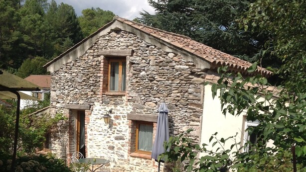 Una casa in pietra con un patio in legno, un tavolino e un ombrellone blu.