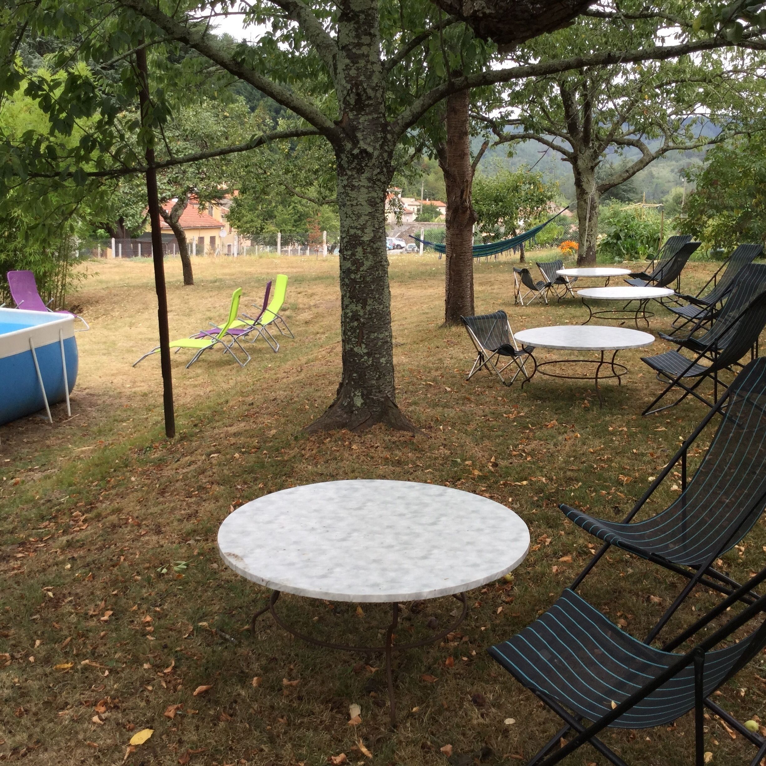 Un espace extérieur aménagé avec des tables et des chaises, entouré d’arbres et d’une pelouse verdoyante.