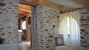 Camera da letto con pareti in pietra, soffitto in legno, un letto e una finestra con tende.