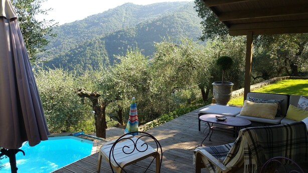 A wooden deck with a pool, lounge chairs, and a view of a mountainous landscape.