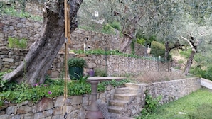 A stone wall garden with a rustic metal table, a large potted plant, and a wooden post.