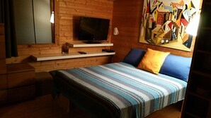 A bedroom with a bed, a TV mounted on a wooden wall, a shelf with a remote, and a painting.