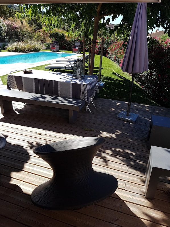 An outdoor patio with a pool, a seating area with a striped tablecloth, and a large umbrella.
