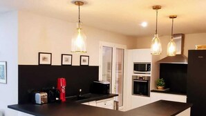 Una cocina moderna con una isla central, taburetes de bar, iluminación colgante y un microondas.
