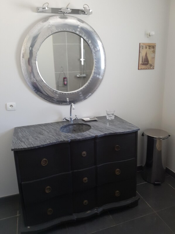 A bathroom with a round mirror, a sink, and a trash bin.