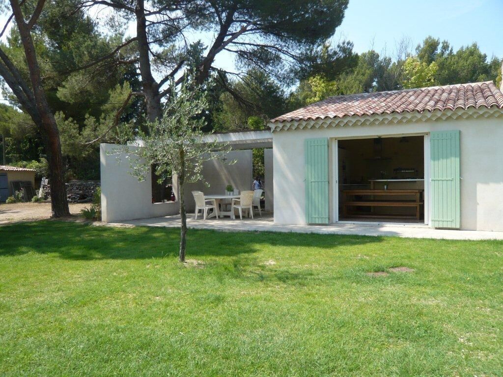Une petite maison avec un toit en tuiles, une terrasse avec une table et des chaises, et un arbre dans la cour.