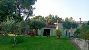 Uma casa com telhado ladrilhado, porta verde e um pequeno jardim com gramado e algumas árvores.